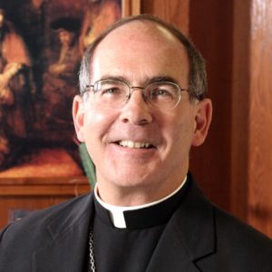 White man wearing glasses in black suit with white clerical collar