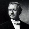 White man with mustache wearing a suit and white bow tie