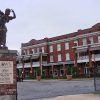 Statue of a dancing girl on brick column outside multistory brick building with parking lot