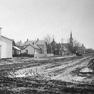 Lumber barn multistory houses and church with steeple on muddy dirt road