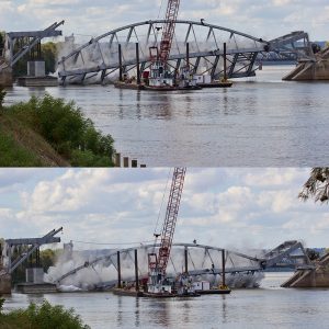 Steel arch bridge being torn down by crane barge on river