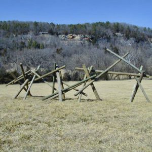 various wooden posts posed at perpendicular angles in a field with a tree covered hill in background