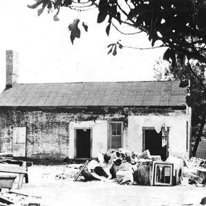 Dilapidated single-story house with debris piled in front yard