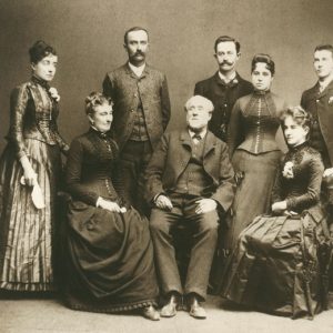 Older white men and women in formal clothes pose with their adult children for family portrait