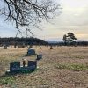 Gravestones and tree in cemetery with tree-covered hills in the background