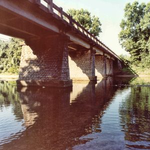 Underside of concrete bridge with stone columns over river