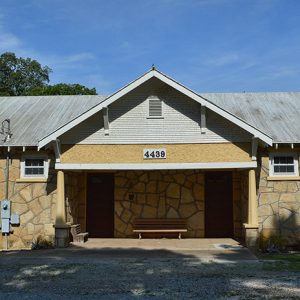 Single-story building with stone walls and two doors under covered porch on gravel