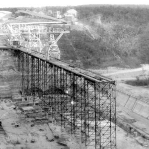 Dry river bed with unfinished dam and cranes with buildings in the distance