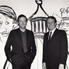 Two white men in suits smiling with caricatures on the wall behind them