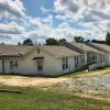 Single-story building with white siding and wheelchair ramp on gravel parking lot in residential neighborhood