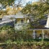 Two-story yellow house with wrap around covered porch fence and trees around it