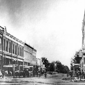 People and cars on city street lined with multistory storefronts