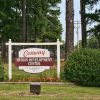 white wooden post sign reading "Conway Human Development Center" amid trees with chain link fence in background