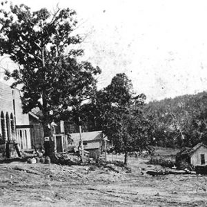 Dirt road with storefronts on both sides and trees