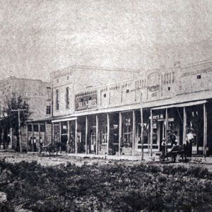 Multistory brick storefronts with covered walkway on dirt road