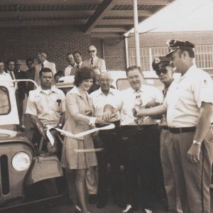 Crowd of white men and women and cars at ribbon cutting ceremony