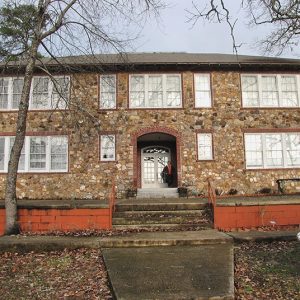 Two-story stone building with arched doorway and steps with brick wall on street