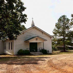 Single-story church building with covered entrance steeple and pavilion in the background