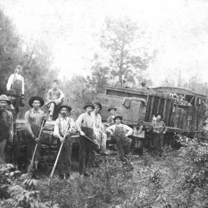 Group of white men, many in overalls, posing with a train while at work