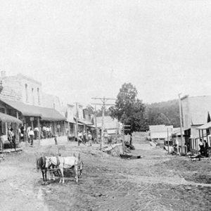 Horses on dirt road between rows of buildings with covered porches in town