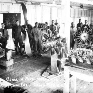 Class of young white men in machine shop posing with various aircraft engines