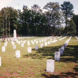 Rows of gravestones in cemetery with stone obelisk monument and flag poles in the background