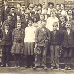 Group of white children and teachers on steps of brick building