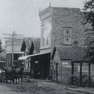 Horse-drawn carriage riding past brick storefronts on dirt road