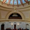 Interior of high ceilinged room with chairs and desks in rows beneath chandelier and stained-glass dome