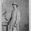 White man in gray military uniform and hat standing with column