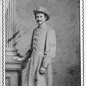 White man in gray military uniform and hat standing with column