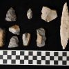 Hand carved stone tools on black background with checkered scale