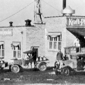 White men with delivery trucks parked outside cheese factory with sign "Kraft-Phenix Cheese Corp"