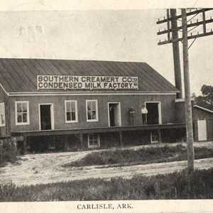 Two men standing on elevated porch of factory building with loading dock and also telephone pole in the foreground