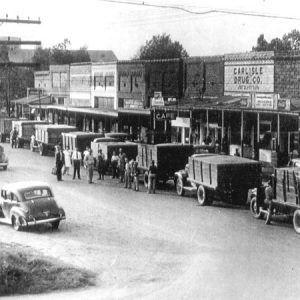 Trucks parked along busy street with men standing around them and cars passing by