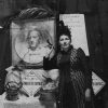 White woman in dress standing next to bust of white man