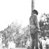 Young African-American man hanging from a pole with white men in hats standing around him