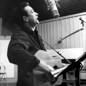 White man playing guitar and singing into a microphone