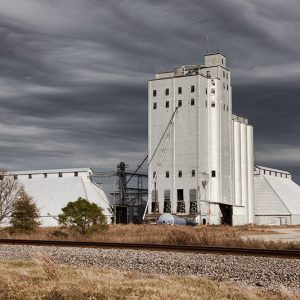 Silver grain elevator and storage buildings under gray skies