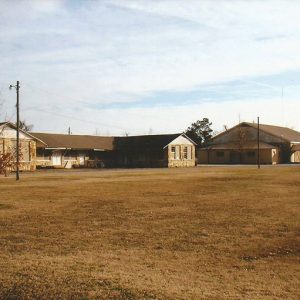 Single-story school building with two wings on grass and larger auditorium in background