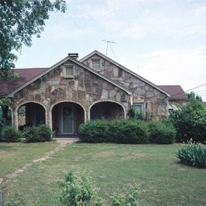 Stone house with arches in front with bushes tree and wooden fence and narrow stone walkway