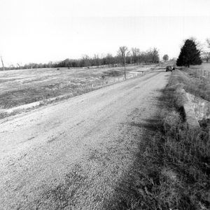 Rural road over creek bridge with truck and trees in the distance