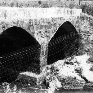 Close-up of stone arch bridge with wire screens in creek