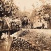 Crowd of white men women and children gathered on bridge over creek with concrete supports