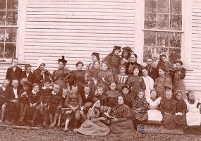 Group of white children and teachers outside school house