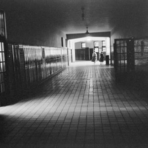 Two teachers walking down an empty school hallway with lockers and a water fountain