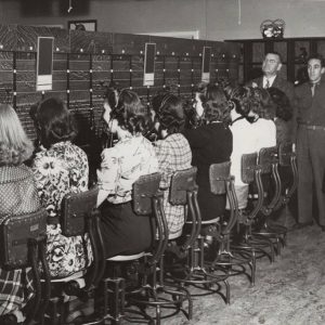 Group of white women sitting at switchboard while white men and woman watch them work