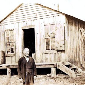 Older white man in suit standing outside single-story building