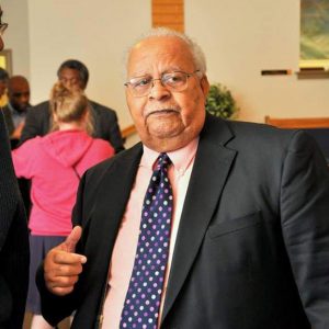 Old African-American man in suit and tie standing in sanctuary with white woman and African-American men standing behind him