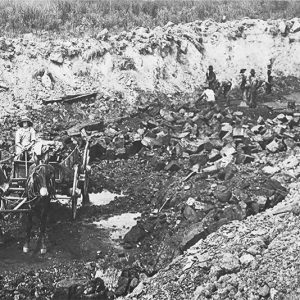 Man riding horse drawn buggy and other men at work in open pit mining area